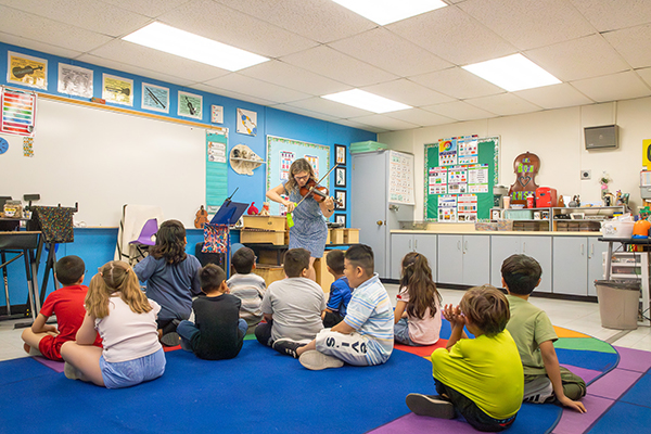 Students sit on the floor while the teacher plays her violin