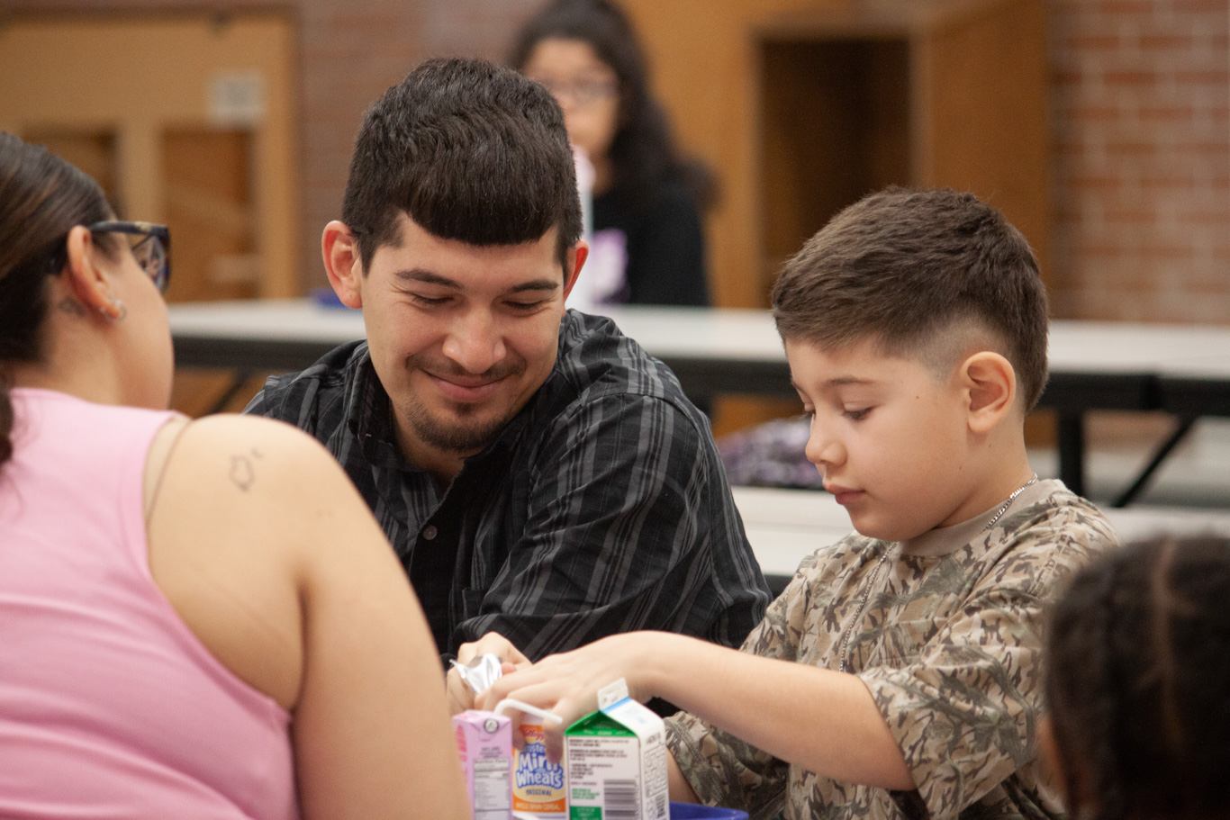 A boy eats breakfast with his parents in the cafeteria