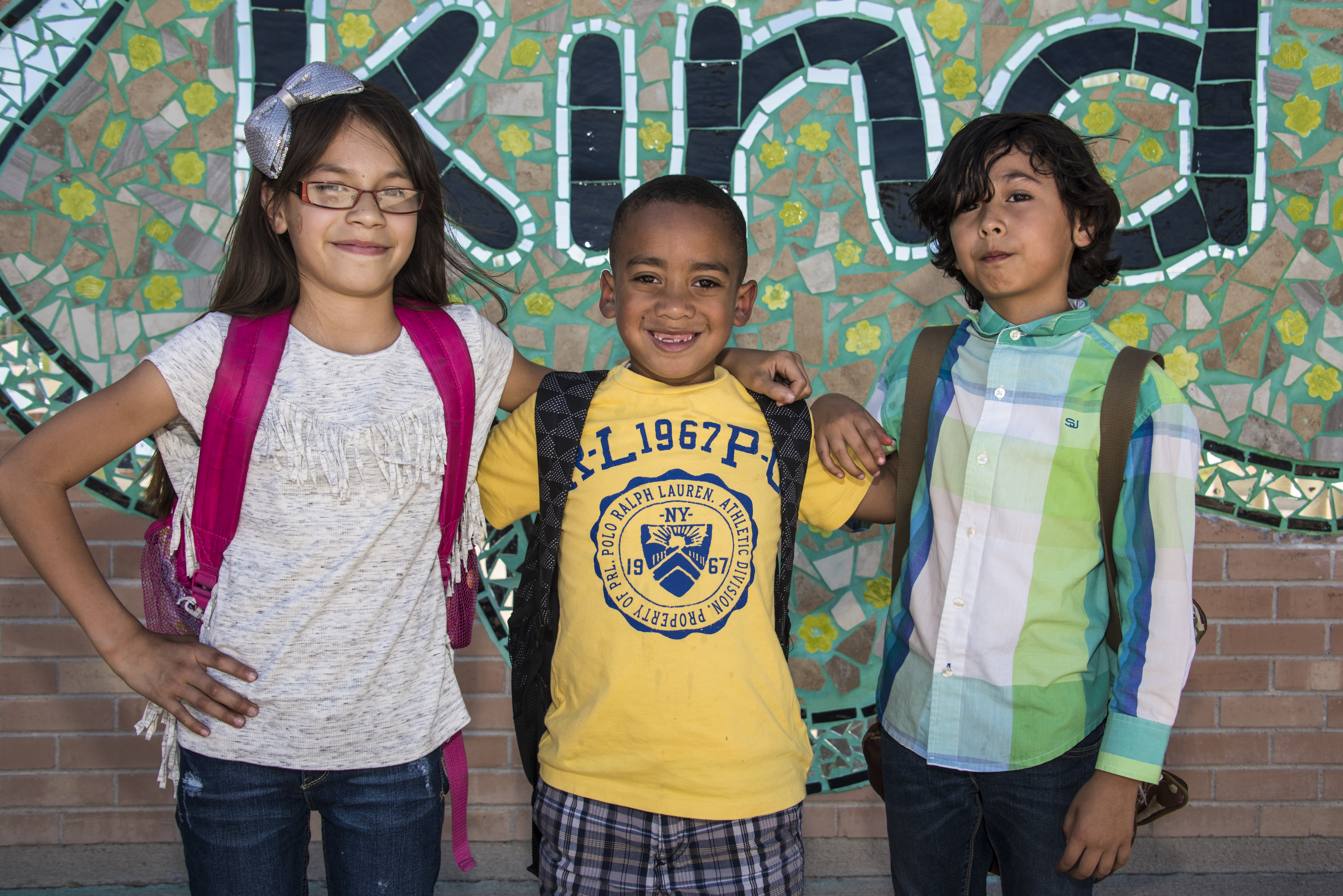 Three friends smile together in front of the Be Kind mural