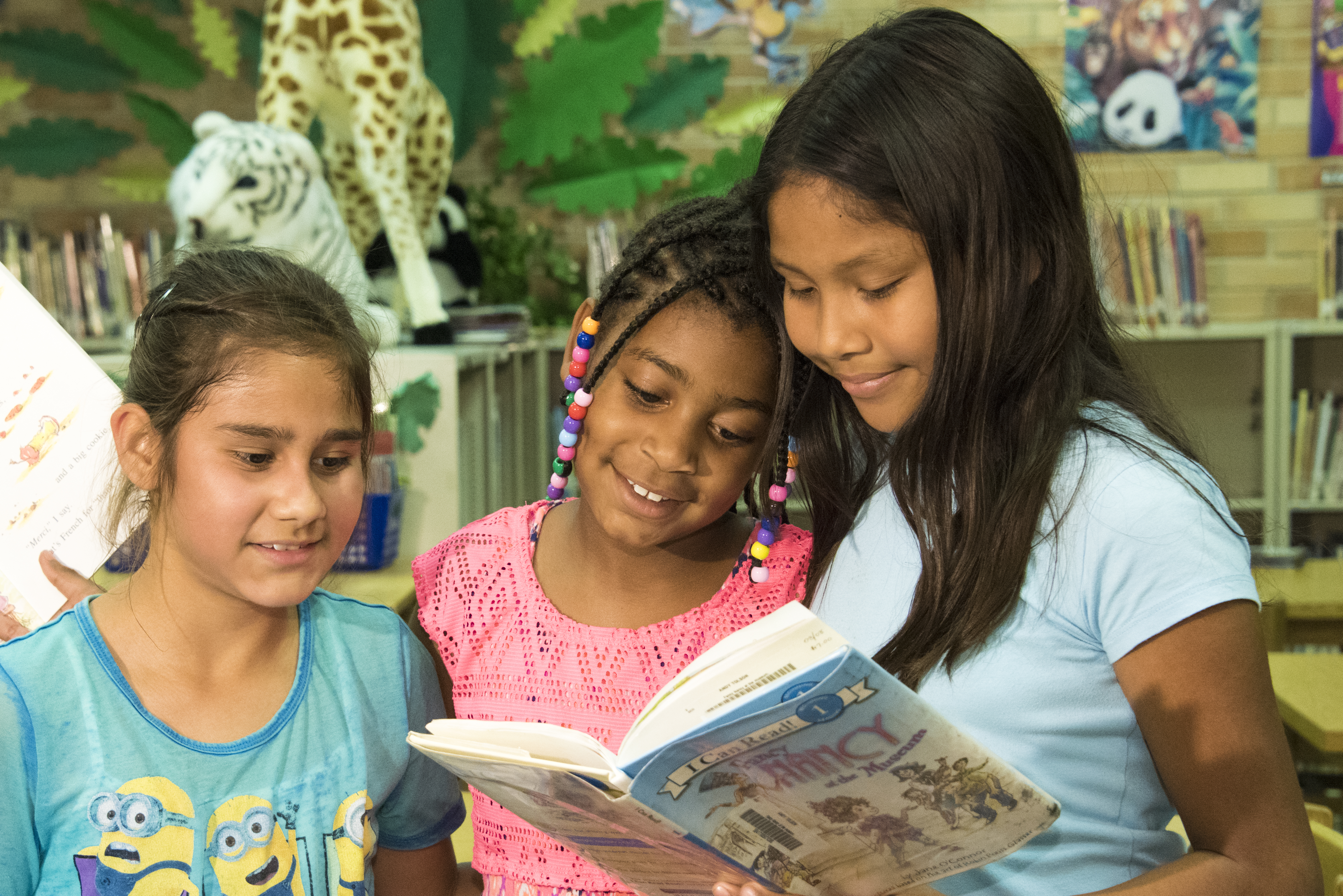 Three girls smile as they read a book together in the library